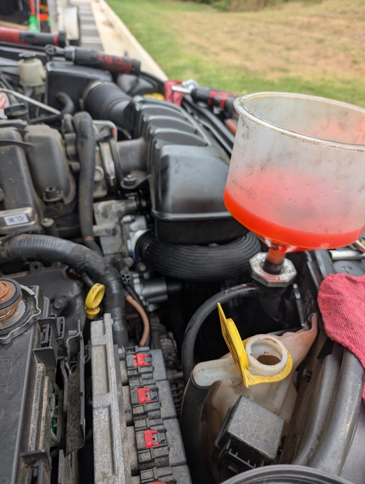 Close view of an engine bay with a funnel of orange coolant feeding into the reservoir