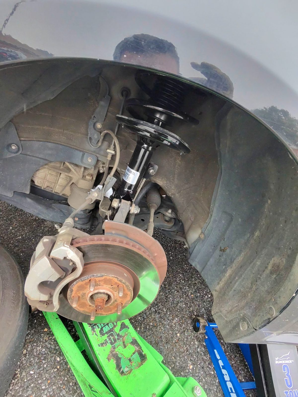 New strut fitted in a front wheel well with the brake rotor and caliper exposed, car on a floor jack
