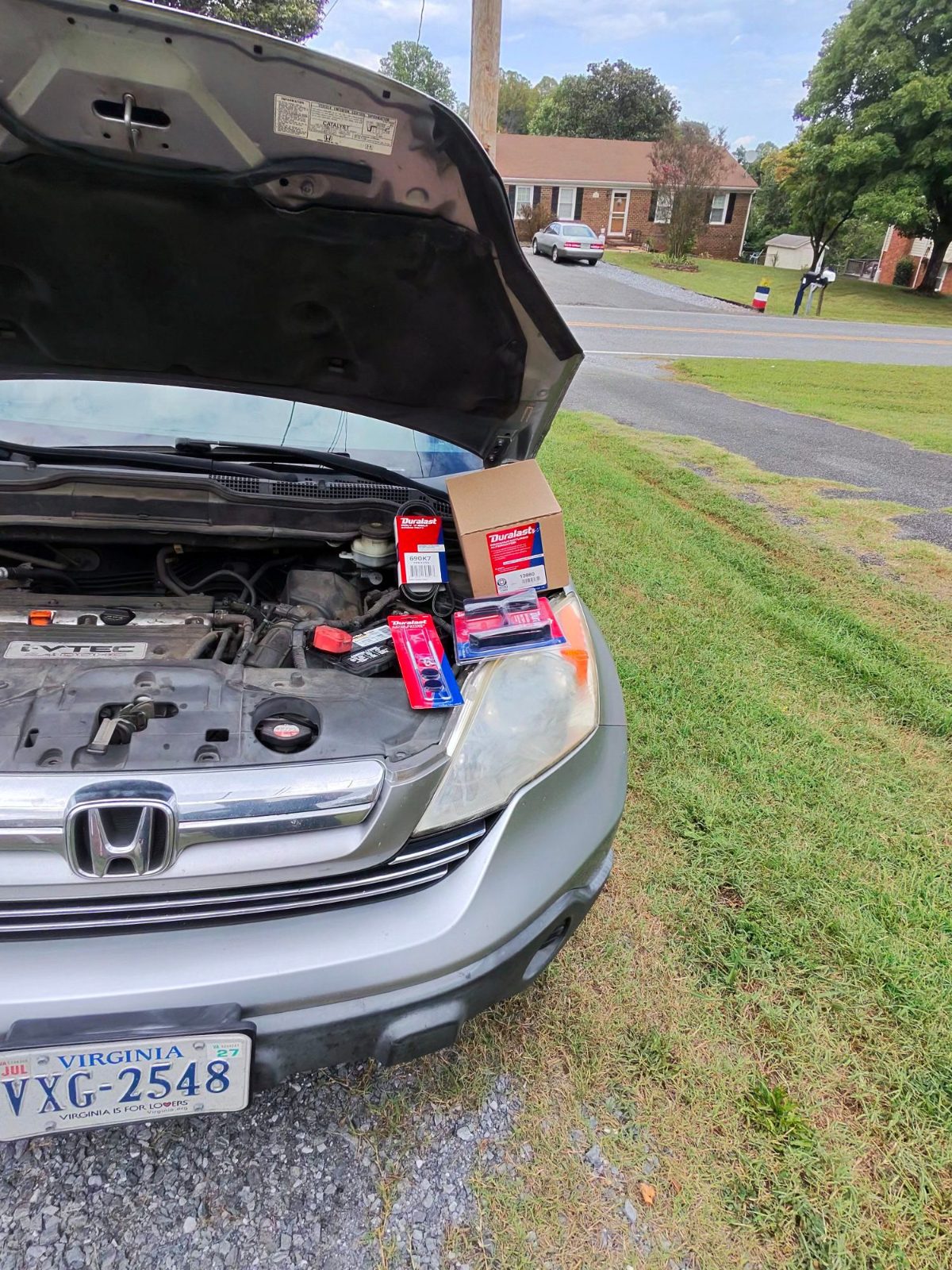 Silver SUV with hood open and new parts in boxes set on the headlight in a driveway